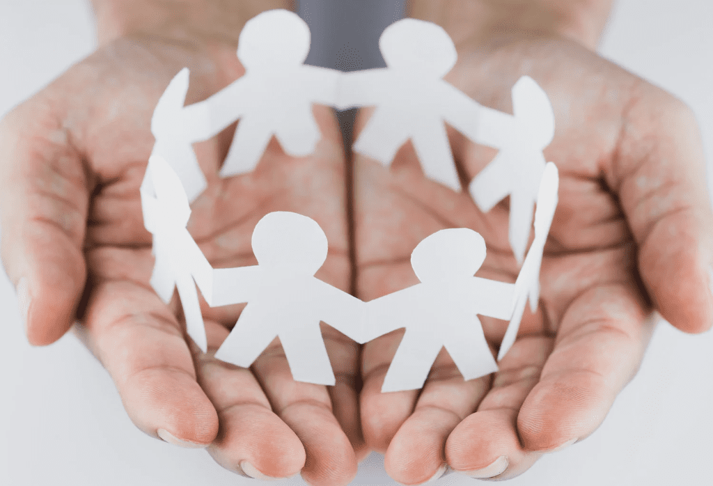 Hands holding a paper chain of human figures, symbolizing community, connection, and support.