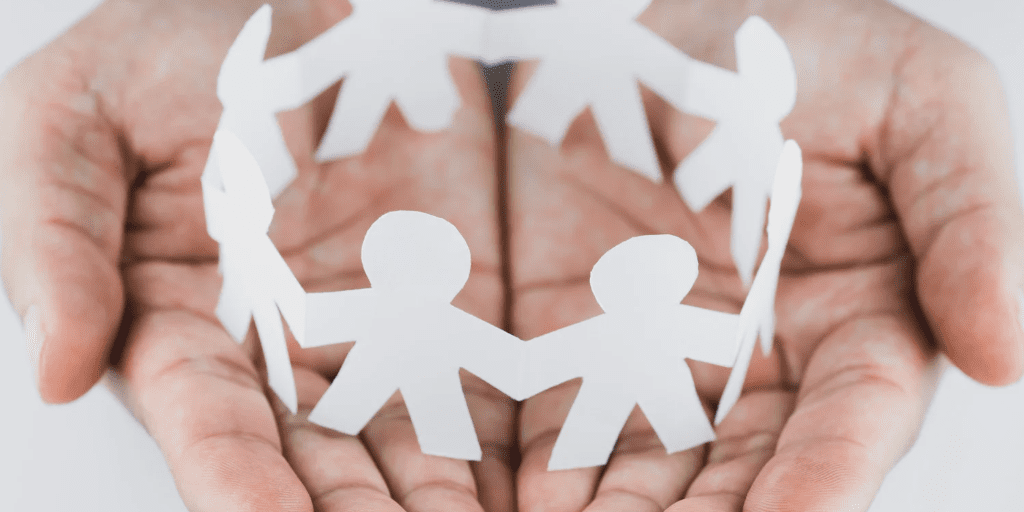 Hands holding a paper chain of human figures, symbolizing community, connection, and support.