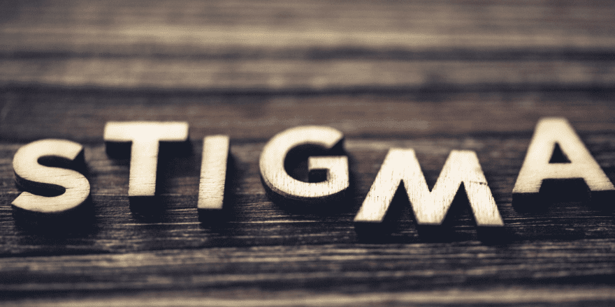 Wooden letters spelling 'Stigma' on a dark wooden surface, symbolizing the concept of stigma related to social issues like substance use and criminal-legal involvement.