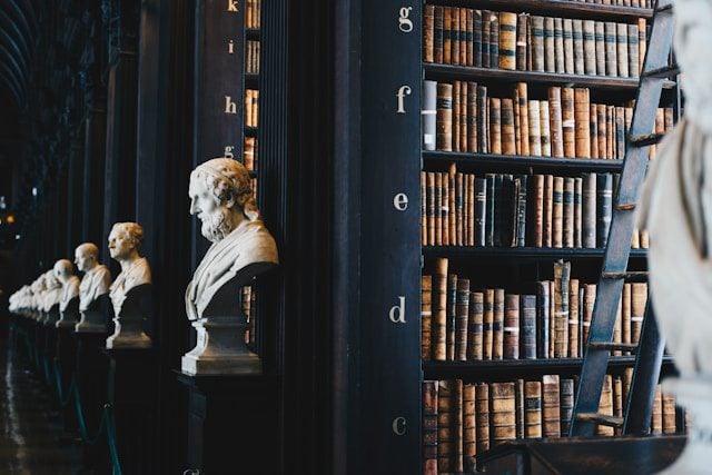 Cropped view of a row of dark bookshelves in a library, each adorned with a bust statue of a literary artist in front